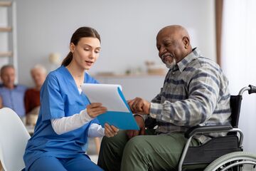 HFH Therapie- und Pflegewissenschaften Bachelor Pflegerin zeigt Patienten etwas auf Klemmbrett