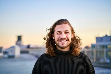 hfh_psychologie_bachelor Mann mit langen Haaren steht auf Hausdach und lacht in die Kamera