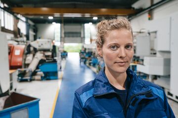 HFH Bachelor Maschinenbau Maschinenbauerin steht in einer Produktionshalle und lächelt in die Kamera