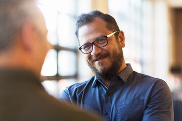 HFH Master Wirtschaftspsychologie Mann mit Hemd und Brille unterhällt sich mit einer anderen Person und lächelt sie an