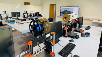 Blick in die "studentische Werkstatt" der Hochschule Heilbronn mit Schreibtischen, Computern, technischen Geräten und großem Monitor an der Wand.