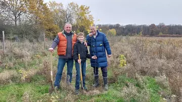 Zwei erwachsene Männer und ein junger Mann stehen auf einem Feld mit Spaten in der Hand.