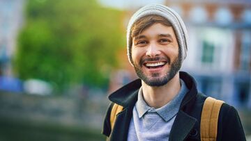 Junger Mann mit Bart und Mütze lächelt in die Kamera.