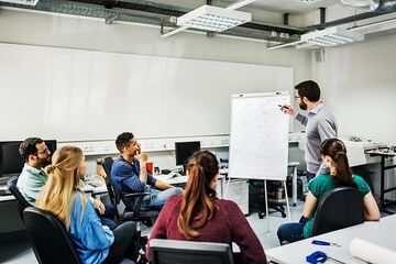 Dozent am Flipchart vor 5 sitzenden Studierenden